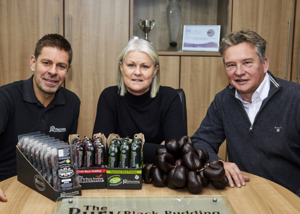 Graham Norfolk Panicium buys Bury Black Pudding Company Pictured l-r Richard Morris The Bury Black Pudding Co Debbie Pierce The Bury Black Pudding Co and new owner Graham Norfolk Panicium